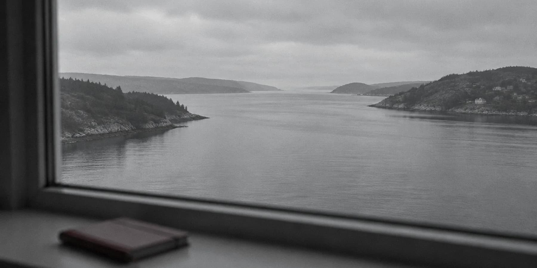 Vista desde una ventana al canal entre dos costas, con un cuaderno rojo desenfocado en el alféizar